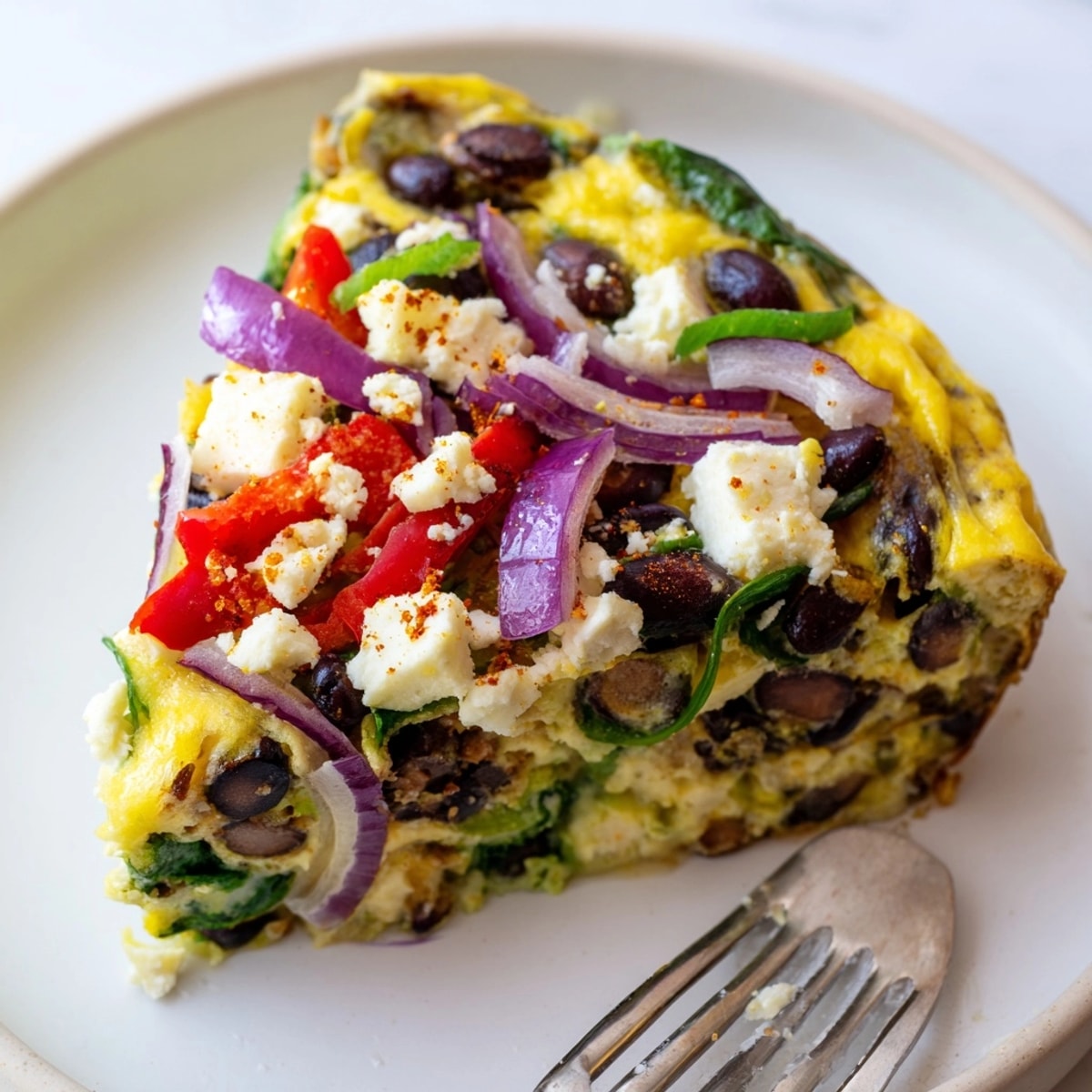 Close-up showcasing a slice of Avocado Black Bean Egg Frittata with creamy avocado chunks.