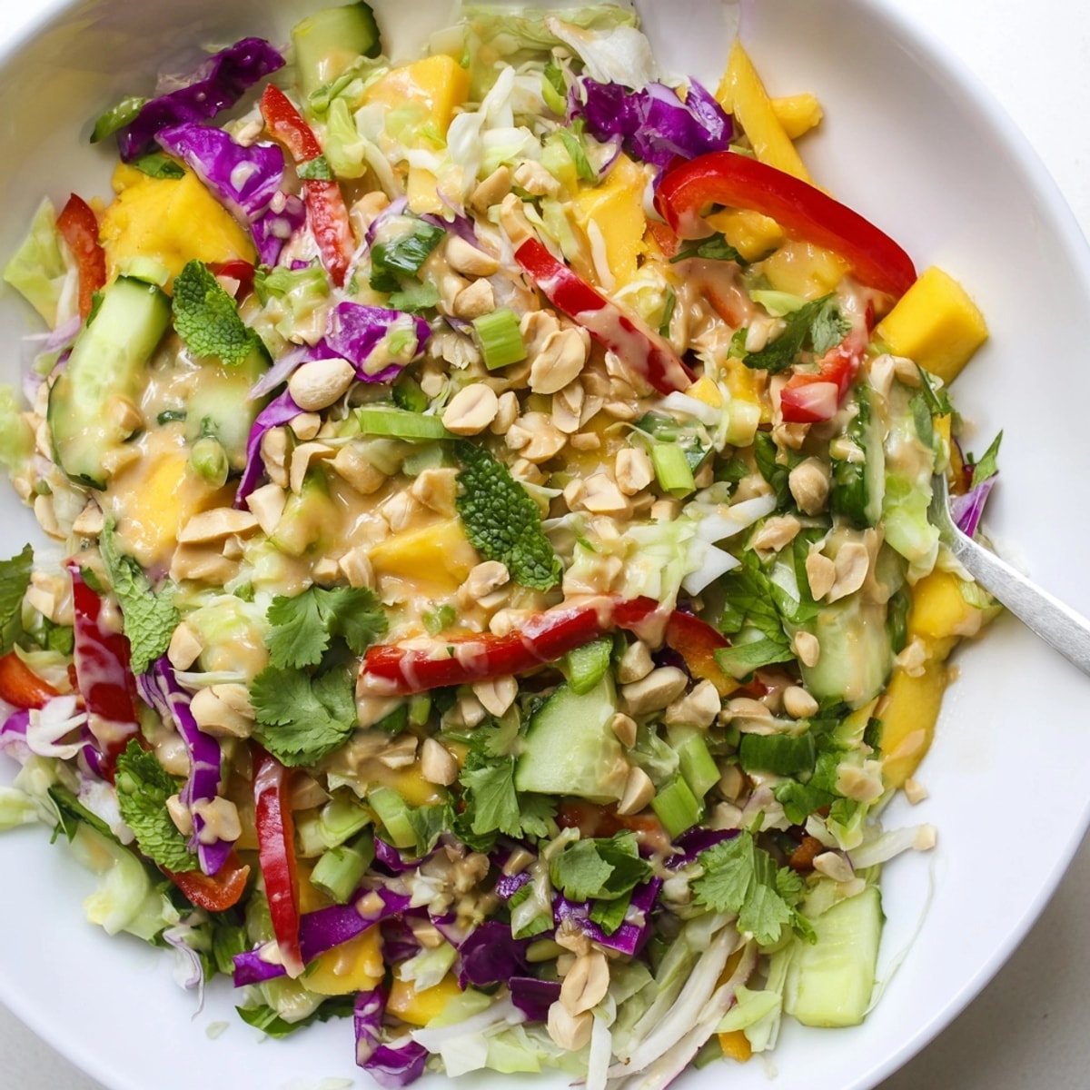Close-up of colorful Thai Peanut Mango Veggie Salad, drizzled with creamy peanut dressing.