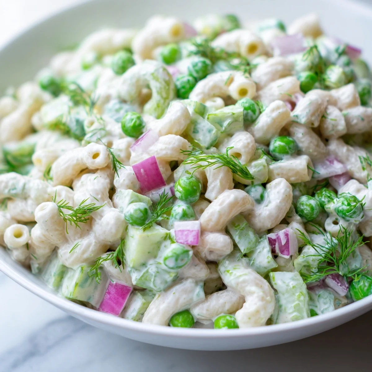 A bowl of creamy dill pickle pasta salad with ditalini, peas, and fresh dill garnish.