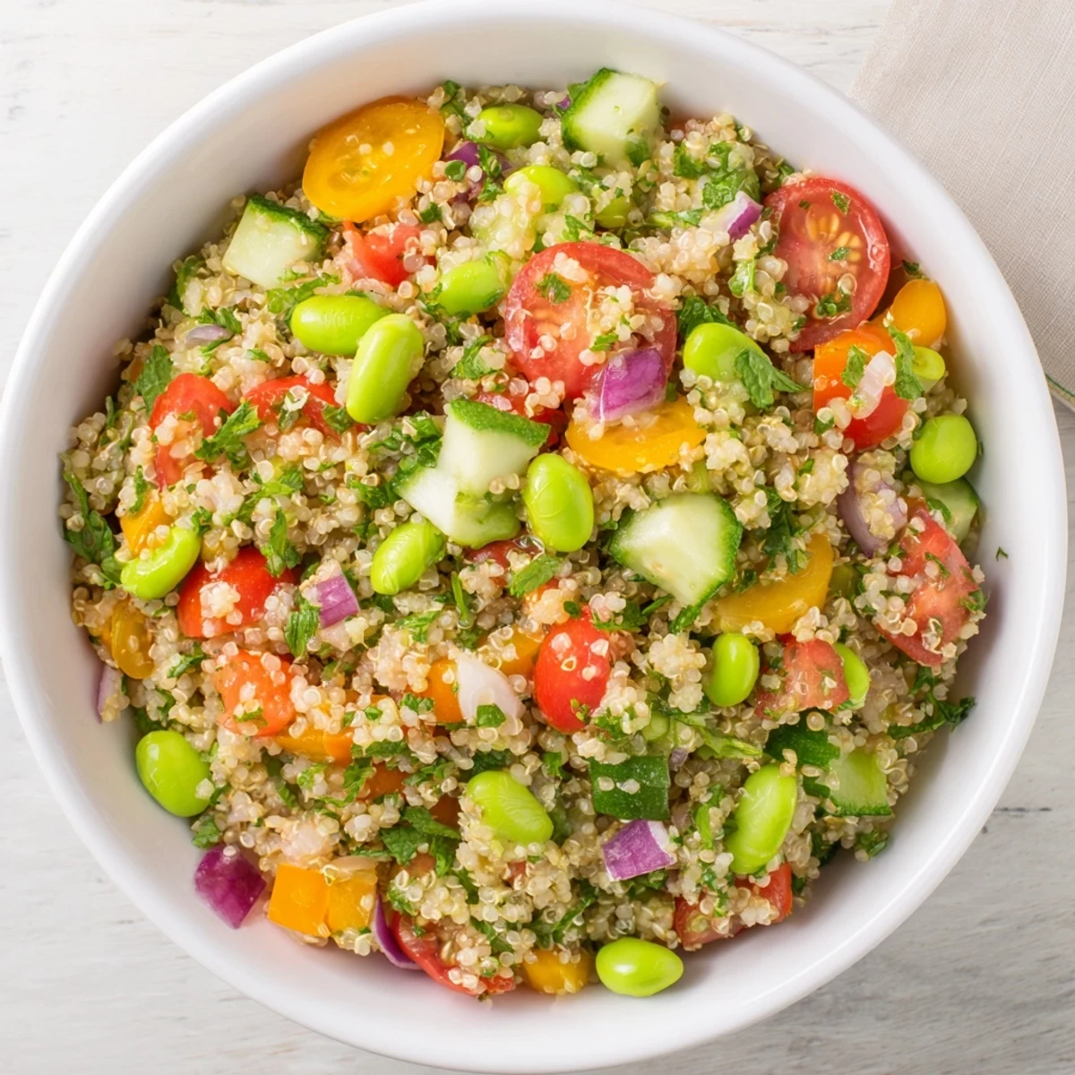 A close-up of Edamame and Quinoa Salad in a white bowl, featuring tender green soybeans, fluffy quinoa grains, and vibrant diced red bell peppers with fresh herbs.