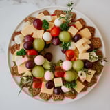 Freshly arranged Jingle Bell Cheese & Cracker Wreath, featuring cubed cheeses, crackers, and holiday sprigs for a party.