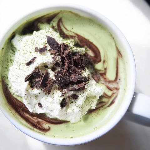 Steaming hot Matcha Hot Cocoa Protein Mug topped with whipped cream, perfect for a cozy afternoon.