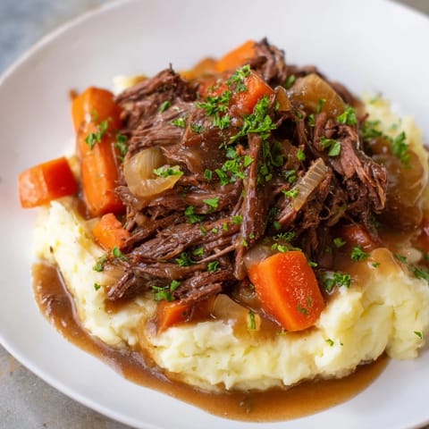 A steaming plate of slow cooker pot roast, rich gravy over flavorful mashed potatoes.
