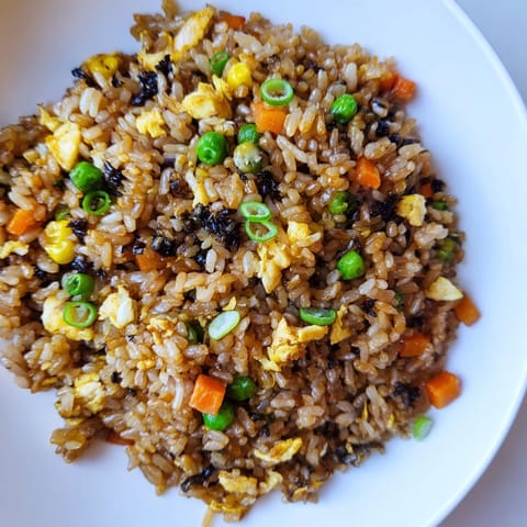 This satisfying skillet of Black Garlic Fried Rice features glistening rice, savory bites, and fresh vegetable garnishes.
