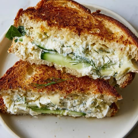 Crisp sourdough bread filled with tangy whipped feta spring grilled cheese and fresh cucumber, stacked on a rustic wooden board.  