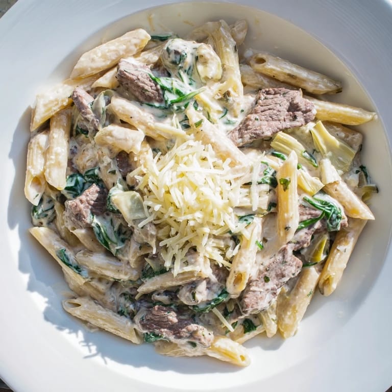 A close-up shot of the savory Steak & Spinach Artichoke Pasta Bake, cheesy and fragrant from the oven.