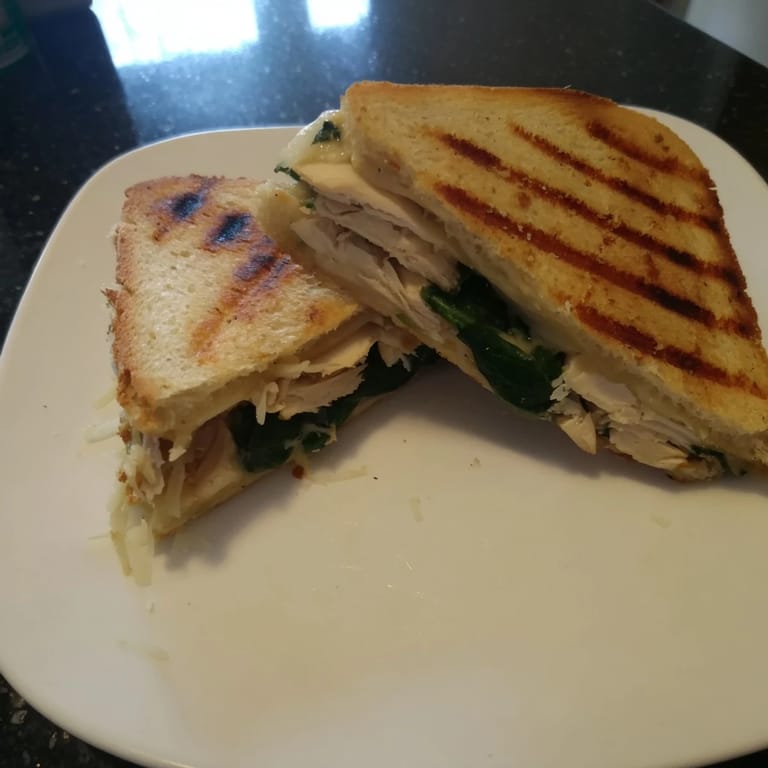 Sliced grilled chicken and fresh spinach tucked inside a warm Grilled Chicken Spinach Panini, pressed until the cheese is perfectly gooey.