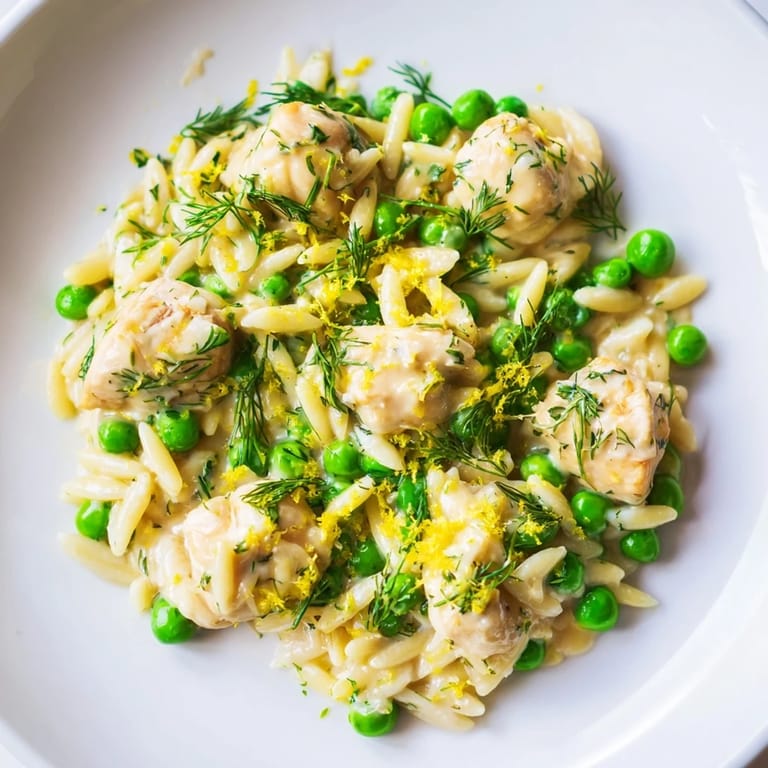 A close-up view highlights the textures of juicy chicken, creamy orzo, and vibrant peas in this easy, weeknight Lemon Herb Chicken Orzo Skillet recipe.