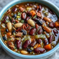 A hearty bowl of 15-bean soup with smoky ham bone, packed with tender beans and savory vegetables for ultimate comfort.